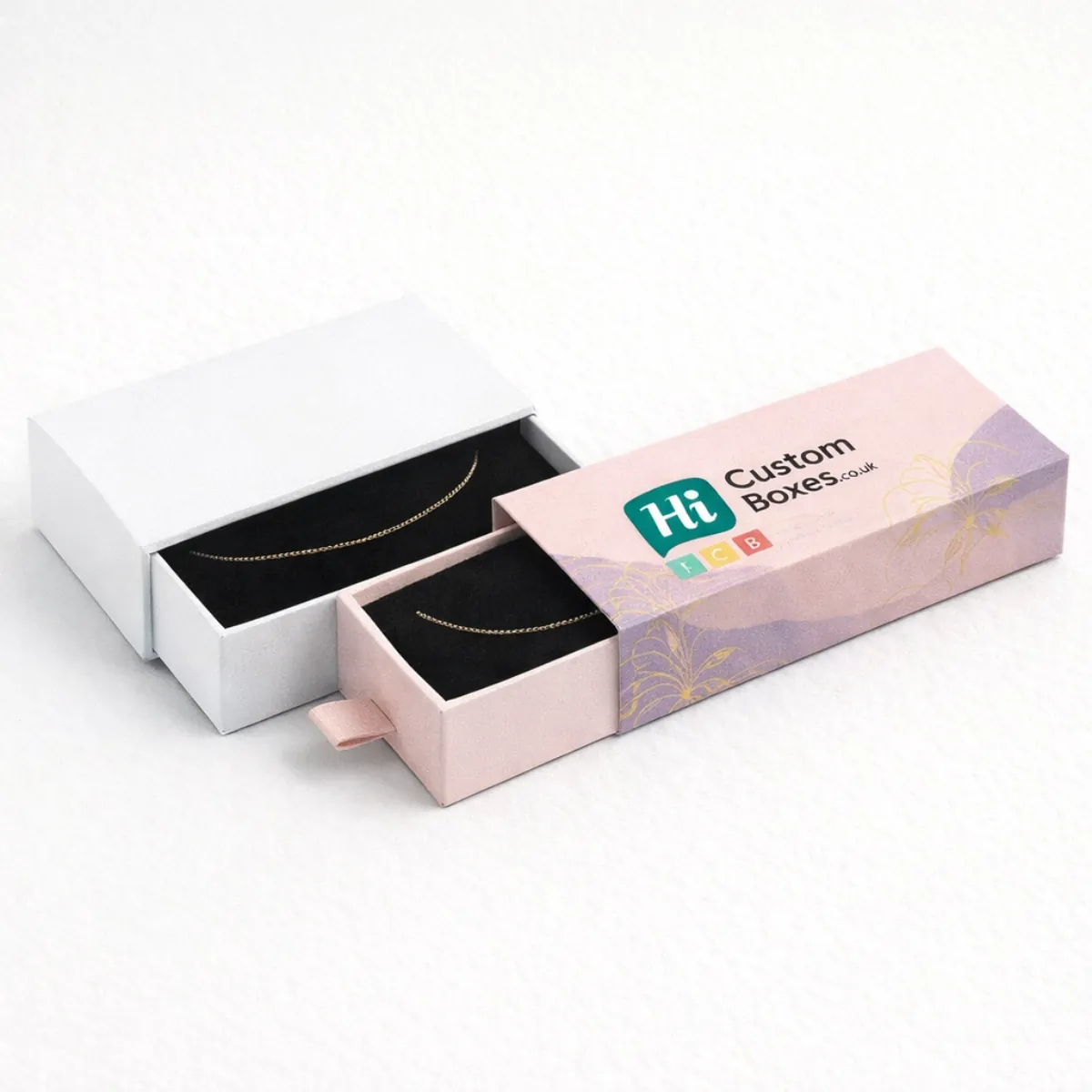 Two premium drawer-style jewellery boxes in white and lilac- featuring gold chain anklets on velvet- class=